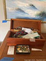 Open wooden jewelry box with various necklaces and bracelets inside, showing a variety of styles and materials.