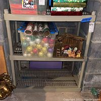 Plastic shelving unit placed in basement against concrete block wall, showing three shelves with grid style lower shelves and solid top shelf. Some dirt and dust visible.