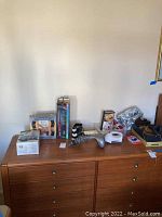 Wide image of various boxed and unboxed massage, hair styling, and accessory items on a wooden dresser surface.