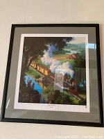 Framed art print of a steam train traveling through a countryside scene with trees, fields, a house, and hills.