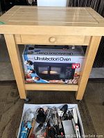 UltraVection Oven in its original retail packaging sitting under a wooden butcher block table, with various kitchen utensils in a drawer of the table.