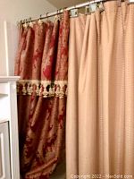 Photo of red decorative shower curtain with floral pattern and gold tassel trim, hanging on metal shower rod.