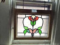 Front view of the stained glass window panel hung on the wall showing the entire floral design and wooden frame.