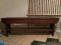 Full front view of bench with lower shelf against wall with pipes in background