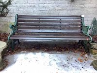 Front view of the full bench against a brick wall showing slatted wood seat and back with green cast iron sides