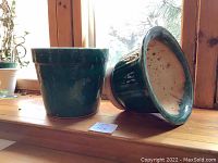 Two green ceramic planters displayed on a wooden ledge with natural light, showing one planter upright and one on its side revealing cream interior and unglazed base.