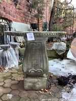 Front view of cement pedestal garden table on brick pavers with scattered leaves and patches of snow