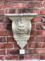 Front view of cement corbel shelf with detailed floral and leaf relief design mounted on brick wall.