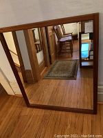Full view of rectangular mirror leaning against wall, showing teak frame and reflective surface.