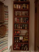 Full view of light brown wooden spice rack mounted on wall with multiple spice jars