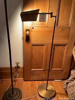 Full view of the brass floor lamp showing base, adjustable arm, and door background