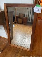 Full view of rectangular teak framed mirror leaning against wall