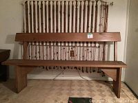 Front view of the old pine church pew showing the full length seating and backrest against a wall with hanging sticks.