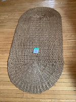 Full view of oval jute rug on hardwood floor showing overall shape and wear