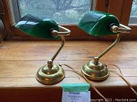 Pair of small vintage bankers lamps with brass bases and green glass shades shown side by side on wooden surface.