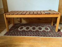 Front view of pine wooden slatted bench on a patterned rug, showing the full length and slatted seat.