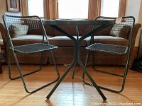 Front view of round table between two mesh chairs on tripod base