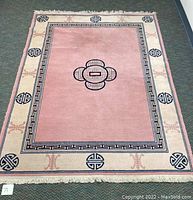 Full view of the Chinese wool rug showing pink central field, geometric medallion, and cream border with symbols.