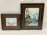 Two framed oil paintings showing nautical and beach scenes on canvas, placed side by side.