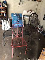 Four metal outdoor chairs, three black and one red, positioned in a garage with visible rust and weathering, surrounded by various items.