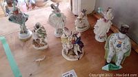 Group photo showing 7 figurines of dancers and a man in a top hat on wooden surface
