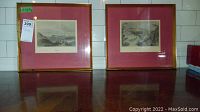 Two framed landscape prints side by side on a tiled wall shelf, showing red mats and gold frames.