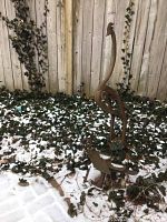 Tall crane sculpture standing upright against wooden fence in snow and ivy.