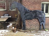 Front left view of black metal horse silhouette leaning against brick wall