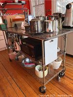 Front view of marble top island showing metal frame, two wire shelves, and caster wheels