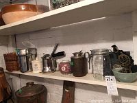 Side view showing array of jars, bowls, metal containers, and decorative items arranged on shelf against white wall.