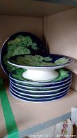 Stack of six decorative plates with one pedestal plate on top, showing leaf pattern and cobalt border