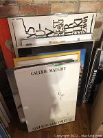 Stack of multiple posters mounted on foam core leaning against brick wall