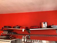 Upper shelves holding a variety of pots, pans, bakeware, and trays against a red wall.
