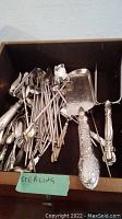 Overview of assorted sterling silver flatware and serving pieces in drawer including iced tea spoons, crumb scoop server, carving fork, sugar shell spoon, sugar tongs and mother-of-pearl butter knife