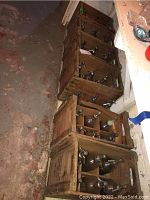 Four wooden crates arranged on basement floor, each holding multiple glass seltzer bottles with metal siphon tops.