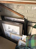 Photo showing multiple framed prints leaning against wall including a Henri Matisse print and black and white cityscape drawing.