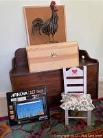 Photo of Arnova 10 G2 tablet box, toy box, doll chair, framed bulletin board behind them, decorative metal rooster sculpture, and hinged wooden box arranged on a carpet