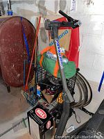 Photo showing Park Tool bike rack leaned in basement with multiple bike tires stacked behind, green fabric bag, and boxed Bell helmet on floor.