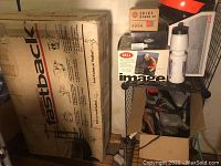 Photo showing Vakima Fastback bike rack in original box and various biking gear on shelving including helmets, bike shoes, knee pads, and water bottle.