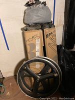 Biking gear showing carbon fiber rims in front of storage boxes with plastic bag and cycling shoes on top