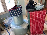 Wide shot showing two large rolls of clear bubble wrap, the hummingbird feeder placed atop the rolls, and the small cardboard drawers with items on top.