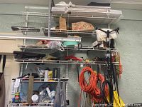 View of six wall-mounted wire shelves with assorted extension cords, tools, boxes, and cleaning supplies in a garage environment.