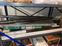 Shelves containing rolls of fiberglass screening, plastic sheeting, and various tubes and rods mainly in black and white colors.