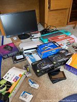 Photo showing lot contents including AOC monitor, boxes of printer ink, Mio GPS, keyboard in box, Compaq USB hub, and other computer accessories.