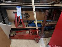 Shelf with red and blue hydraulic floor jacks and two red jack stands, set against a cardboard backing with Blitz branding.