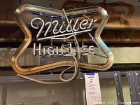 Miller High Life neon bar sign with cursive 'Miller' and block 'HIGH LIFE' inside a neon border frame, not powered on and cords visible.