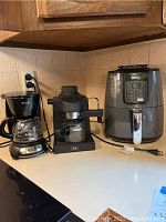 Three kitchen appliances on countertop: left Mr. Coffee 5-cup coffee maker, center Melitta espresso machine, right Ninja air fryer.