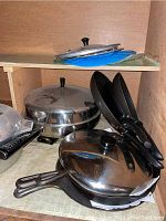 Photo showing multiple covered pots with black handles and stainless steel lids, some cast iron cookware.