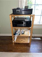 Full view of the pine 4 tier shelf holding the Onkyo amplifier, Yamaha cassette deck, remotes and extension cords.
