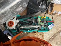 Wide view of the green sled filled with a Stihl leaf blower, hedge trimmer, bike pump, fishing net, spray can, and yellow tool.